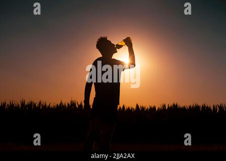 Silhouette des Menschen bei Sonnenuntergang trinkt der Mensch ein Wasser. Stockfoto