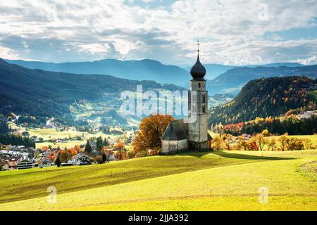 St. Valentin (Kastelruth) Dorfkirche in den herbstlichen Dolomiten. Herrliche Landschaft mit kleiner Kapelle auf sonniger Wiese und schneebedecktem Petz-Gipfel in der Gemeinde Kastelruth. Dolomiten, Südtirol, Italien Stockfoto