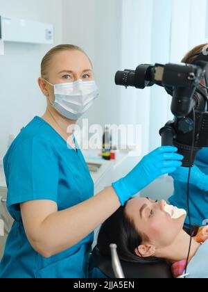 Weibliche Zahnärztin mit dem Zahnmikroskop Behandlung von Patientenzähnen in der Zahnarztpraxis. Medizin, Zahnmedizin und Gesundheitswesen Konzept. Zahnärztliche Ausrüstung Stockfoto