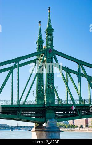 Die Freiheitsbrücke, auch bekannt als Freiheitsbrücke, steht mit Türmen gegen den blauen Himmel in Budapest, Ungarn. Die Donau fließt darunter. Stockfoto