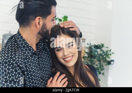 Nahaufnahme eines jungen erwachsenen, verheirateten heterosexuellen Paares, das in der Küche lächelt, lacht und kuschelt. Hochwertige Fotos Stockfoto