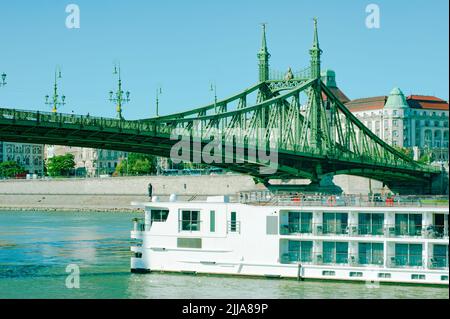 Flusskreuzfahrtschiff fährt unter der Freiheitsbrücke auf der Donau in Budapest, Ungarn. Die Brücke ist auch als Freiheitsbrücke bekannt. Stockfoto
