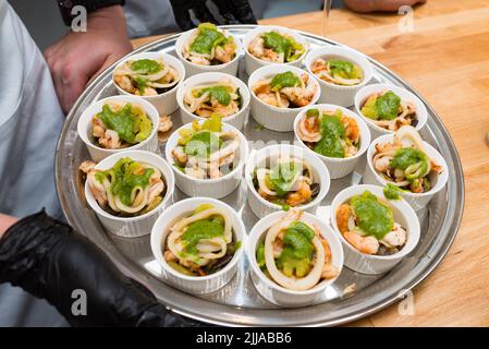 Meeresfrüchte mit Pesto-Sauce in Ramekins auf einem Metalltablett. Viele Portionen. Stockfoto