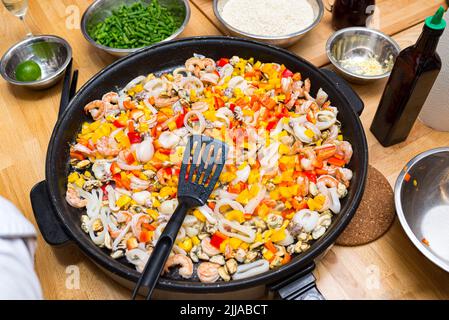 Meeresfrüchte in einer Paella-Schale (Paella-Pfanne) mit gehackten Paprikastückchen gebraten. Meeresfrüchte-Cocktail. Garnelen, Tintenfische, Kraken, Muscheln. Stockfoto