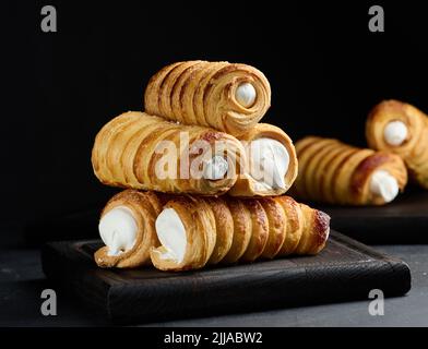 Gebackene Tubuli mit Schlagproteincreme auf einem Holzbrett, schwarzer Hintergrund Stockfoto