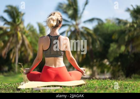 Eine junge Frau praktiziert Yoga an der Meeresküste während des Sonnenaufgangs. Stockfoto