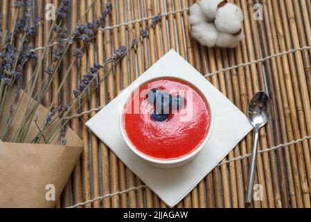 Panna Cotta mit Himbeer-Coulis. Das Dessert wird mit Heidelbeeren garniert. Eine Portion für einen auf einer Matte. Stockfoto