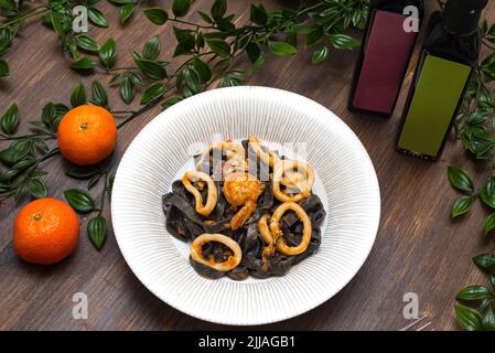 Schwarze Pasta mit Tintenfisch-Tinte und Meeresfrüchten (Garnelen und Tintenfischringe). Eine Portion etwas oberhalb der Ansicht. Stockfoto