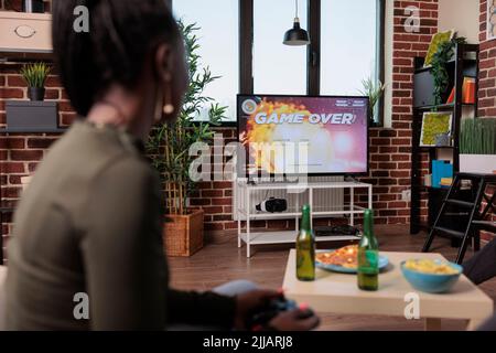 Weibliche Spieler verlieren nach dem Spielen Shooter-Videospiele, frustriert über verlorene Konkurrenz. Traurige verärgerte Frau, die Spielkonsole benutzt, um ein Schießspiel zu spielen, Strategie verliert beim Sammeln. Stockfoto