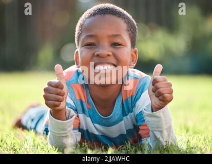 Ich habe heute so viel Spaß. Ein kleiner Junge liegt draußen auf dem Gras. Stockfoto