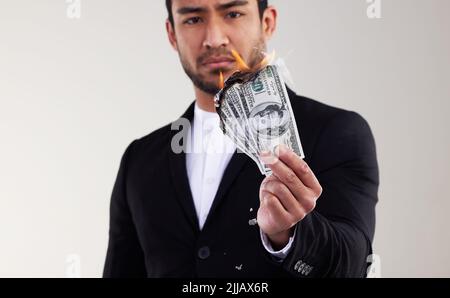 Geld ist die Wurzel allen Übels. Studioaufnahme eines jungen Geschäftsmannes, der vor weißem Hintergrund eine Banknote verbrennt. Stockfoto