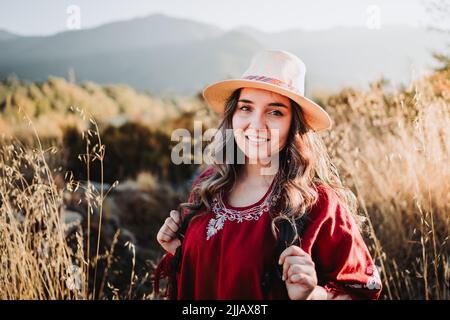 lateinamerikanische Backpacker-Frau in einem traditionellen roten Poncho und einem Hut in einem sonnigen natürlichen Raum Stockfoto