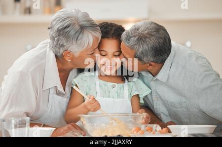 Die süßesten Wangen der Welt. Zwei Großeltern küssen ihr Enkelkind beim Backen auf die Wange. Stockfoto