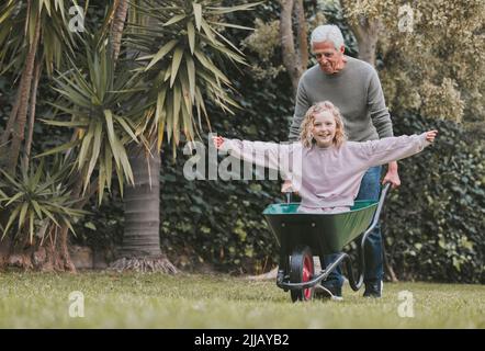 Unsere liebsten Kindheitserinnerungen sind voller Spaß. Ein entzückendes kleines Mädchen, das Spaß mit ihrem Großvater in einem Garten hat. Stockfoto