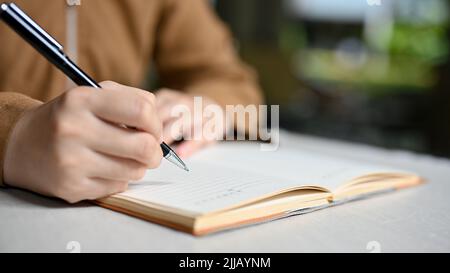Eine Studentin oder Schülerin, die ihre Hausaufgaben auf einem Schulnotizbuch schreibt. Weibliche Hand schreibt auf ihr Tagebuch. Nahaufnahme und Scharfstellung von Handbildern Stockfoto