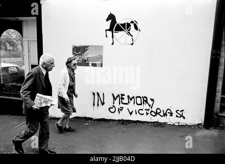 Ein älteres Paar, Bewohner von Kings Cross in Sydney, das mit aktivistischen Green Ban-Graffiti in einer der Seiten spaziert. Mann, der Zeitung mit Schlagzeile trägt, Arab Bloodbath. Vintage-Foto Stockfoto