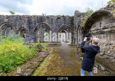 Whalley Abbey Ruinen und Gelände Sommer 2022, weibliche Besucher Modell veröffentlicht nutzt iPhone, um Fotos von den Ruinen zu machen, Whalley, Lancashire, England, Großbritannien Stockfoto