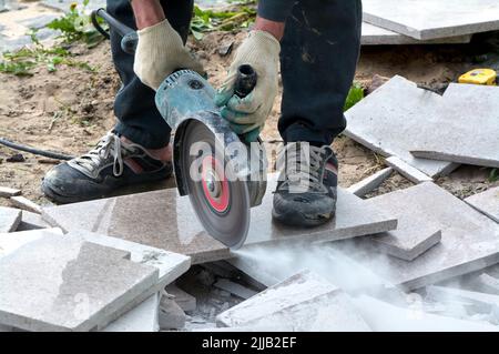 Ein Arbeiter mit einer Kreissäge schneidet in Nahaufnahme eine Fliese. Stockfoto