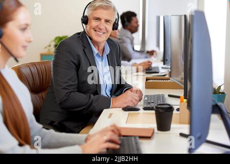 Es war ein guter Tag, um große Umsatzziele zu erreichen. Porträt eines reifen Call Center-Agenten, der zusammen mit seinen Kollegen in einem Büro arbeitet. Stockfoto