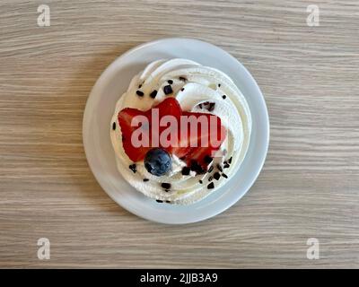 Pawlova-Dessert auf Meringuebaske mit Schlagsahne und Schokolade, Erdbeerscheiben und Blaubeerdekor. Der Kuchen ist nach der russischen Ballerina benannt Stockfoto