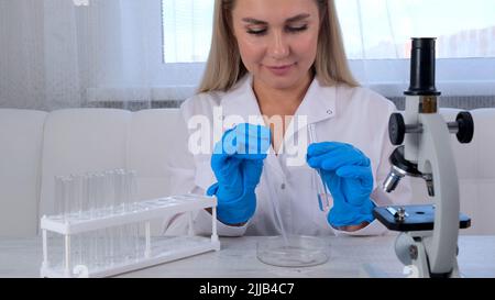 Forscherin Chemikerin in einem medizinischen Anzug und Schutzhandschuhen erforscht Proben mit einer Mikropipette und Reagenzgläsern für die Arbeit Stockfoto