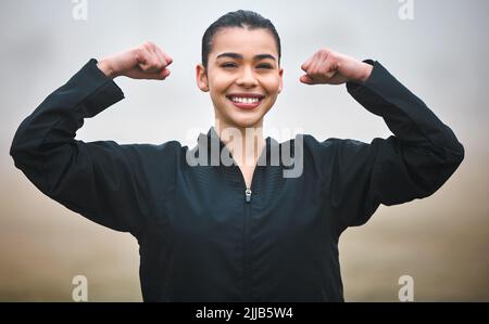 Dezenter Flex. Beschnittenes Porträt einer attraktiven jungen Sportlerin, die ihren Bizeps beugt, während sie draußen steht. Stockfoto