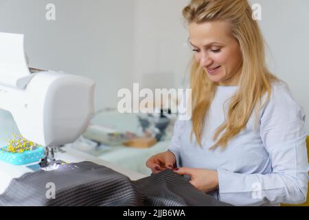 Näherin Frau arbeitet an Nähmaschine. Schneiderarbeitsplatz. Maßgeschneiderte Arbeit zu Hause Stockfoto