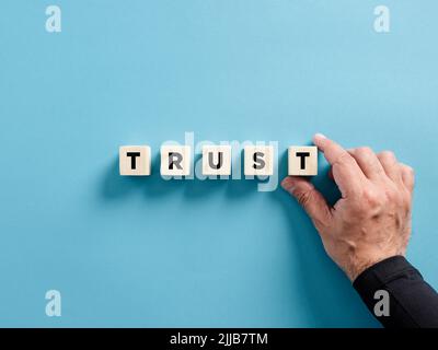 Male hand placing the wooden cubes with the word trust. Business trust concept. Stockfoto