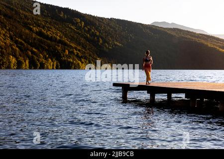 Touristenfrau, die an einem wunderschönen Sommertag auf einem hölzernen Pier auf dem Millstätter See in Kärnten, Österreich, spaziert Stockfoto