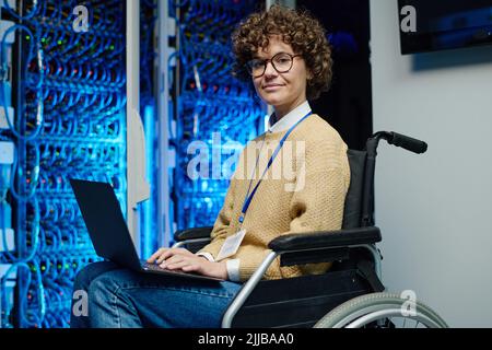 Porträt einer IT-Ingenieurin, die im Rollstuhl sitzt und online an einem Laptop arbeitet, der Server im Rechenzentrum verwaltet Stockfoto