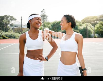 Die gemeinsame Zeit auf dem Platz macht so viel Spaß. Zwei sportliche junge Frauen machen nach dem Tennisspielen auf einem Platz eine Pause. Stockfoto