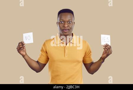 Der verwirrte afroamerikanische Mann zögert hinsichtlich der Wahl, die er treffen muss, und der richtigen Entscheidung. Stockfoto