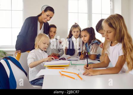 Eine Gruppe von Erstklässlern lernen unter Anleitung einer freundlichen Lehrerin zu schreiben und zu lesen. Stockfoto