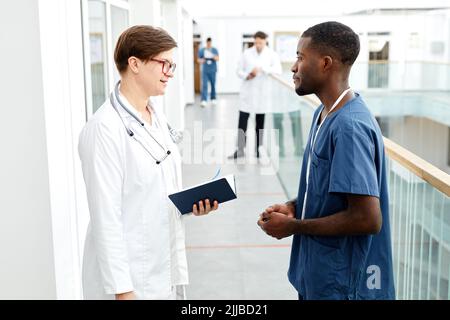 Seitenansicht Porträt einer Ärztin, die mit einem Assistenten spricht, während sie in der Halle einer modernen Klinik steht Stockfoto