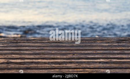 Alte Holzbretter und verschwommener Strand auf der Rückseite. Leerer Holzsteg für Hintergrund mit Platz für Text. Stockfoto