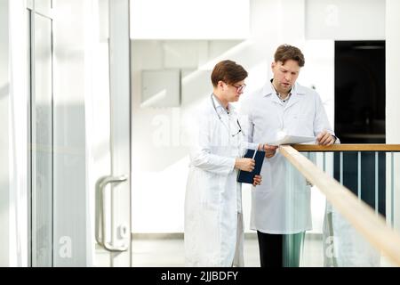 Minimales Porträt von zwei fachkundigen Ärzten, die den Fall in der Halle der modernen Klinik in weißen Tönen diskutieren, Kopierraum Stockfoto