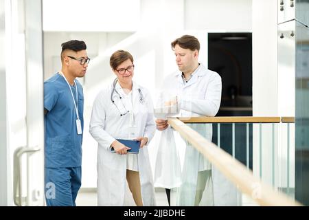 Gruppe von erfahrenen Ärzten diskutieren Fall in der Halle der modernen Klinik in weißen Tönen, Raum kopieren Stockfoto