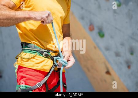 Ein Kletterer strickt einen Knoten. Ein Mann bereitet sich darauf vor, eine Kletterroute zu besteigen. Versicherung und Sicherheit beim Klettern. Stockfoto