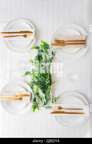 Tischdekoration für festliches Dinner mit weißen Porzellantellern, Gläsern, dekorativem Textil und Besteck. Geschirr Hintergrund in Weißgold Ton. Stockfoto