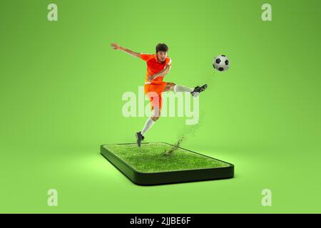 Kreative Collage. Professioneller männlicher Fußballspieler, der auf dem 3D-Telefonbildschirm auf grünem Hintergrund Fußball spielt. Sport, Erfolge, Medien, Online Stockfoto