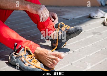 Der Kletterer zieht Kletterschuhe an und bindet Schnürsenkel ein. Vorbereitung auf den Aufstieg. Nahaufnahme der männlichen Hände Stockfoto