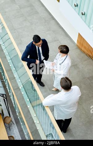 Grafische Ansicht von oben nach unten auf medizinische Fachkräfte, die den Fall besprechen, während sie in der Halle einer modernen Klinik stehen Stockfoto