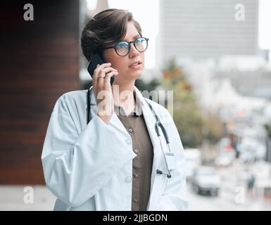 Sie hilft den Patienten auf jede erdenklichen Weise. Eine junge Ärztin auf einem Anruf vor dem Hintergrund einer Stadt. Stockfoto