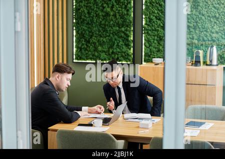 Porträt von zwei erfolgreichen Geschäftsleuten in Anzügen während der Tagung im Konferenzraum im grünen Öko-Design Stockfoto