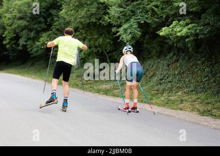 Athletische Frau und Mann trainieren gemeinsam auf dem Rollski. Rückansicht. Konzept von Wettbewerb, Biathlon und Sommertraining. Stockfoto