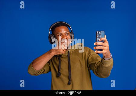 Lächelnder, dunkelhäuter Millenials-Sportler mit Kopfhörern, der Musik auf dem Mobiltelefon auswählt Stockfoto