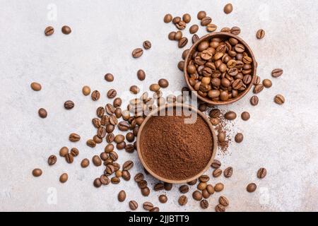 Draufsicht auf geröstete Bohnen mit gemahlenem Kaffee in Schüsseln auf hellgrauem Betonhintergrund Stockfoto