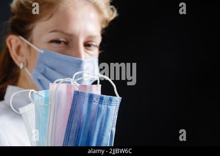 Der Arzt hält mehrere Masken verschiedener Farben in seinen Händen. Eine Krankenschwester, die eine Maske und medizinische Handschuhe trägt, zählt die schützenden Einwegmasken auf einem Stockfoto