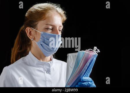 Der Arzt hält mehrere Masken verschiedener Farben in seinen Händen. Eine Krankenschwester, die eine Maske und medizinische Handschuhe trägt, zählt die schützenden Einwegmasken auf einem Stockfoto