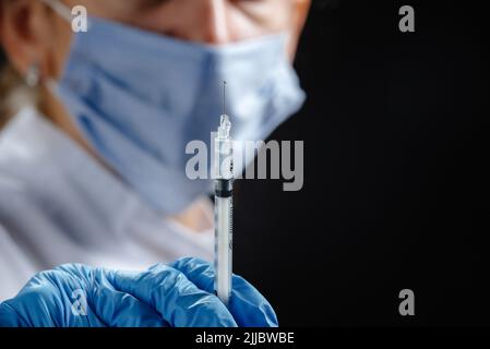 Eine junge Ärztin mit einer Spritze schaut auf die Kamera. Eine Krankenschwester, die eine medizinische Maske und blaue Latexhandschuhe trägt. Medizin und Gesundheitswesen. Impfung Stockfoto